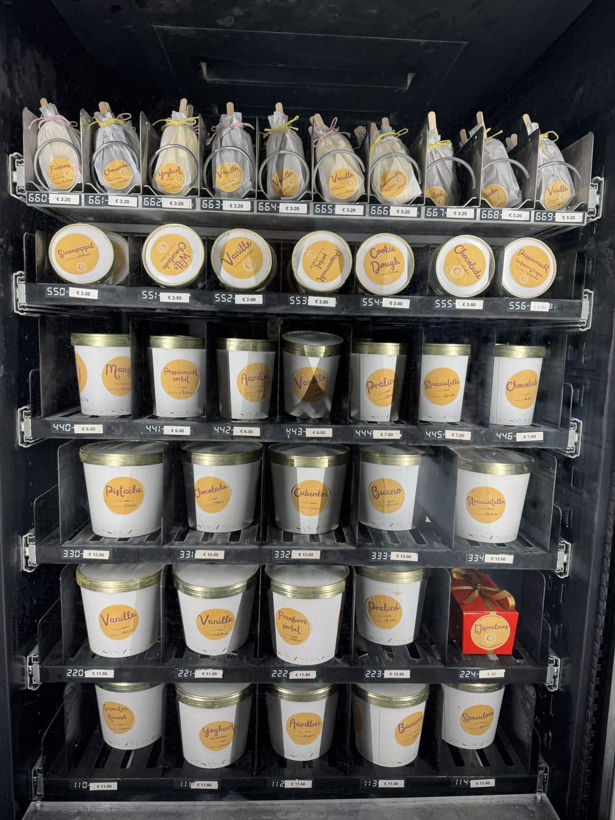 De ijsautomaat van binnen: potjes, liters en frisco's op de schappen, met de prijzen erbij.