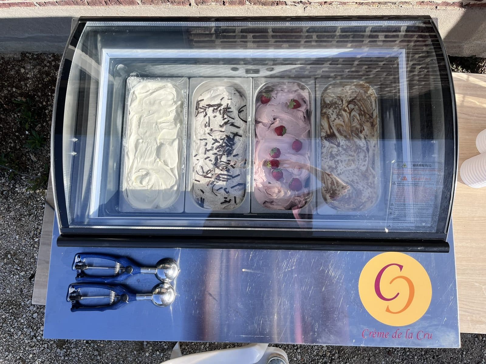 De tafelvitrine van bovenaf, gevuld met vier smaken ijs en met de ijsscheppen erbovenop.